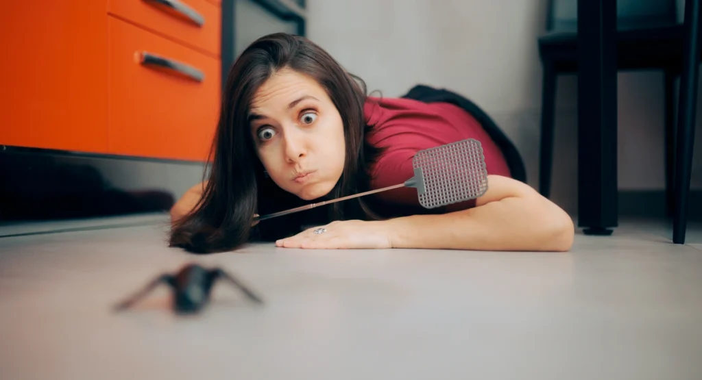 woman on floor trying to slap an insect with a fly swatter