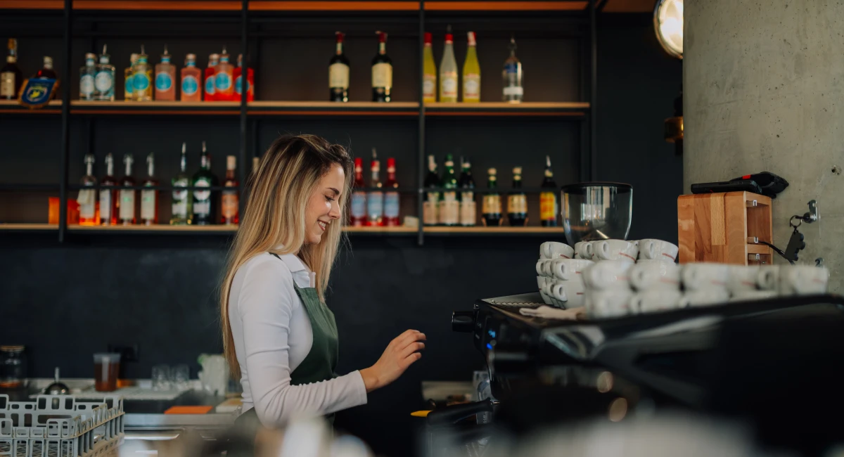 Young barista woman skillfully preparing coffee with a professional machine in a bustling cafe, radiating joy and expertise