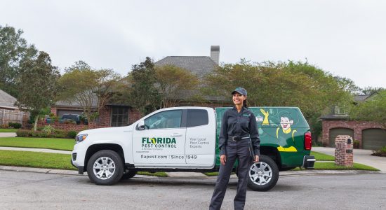 A Florida Pest Control technician stands in front of her branded truck, smiling